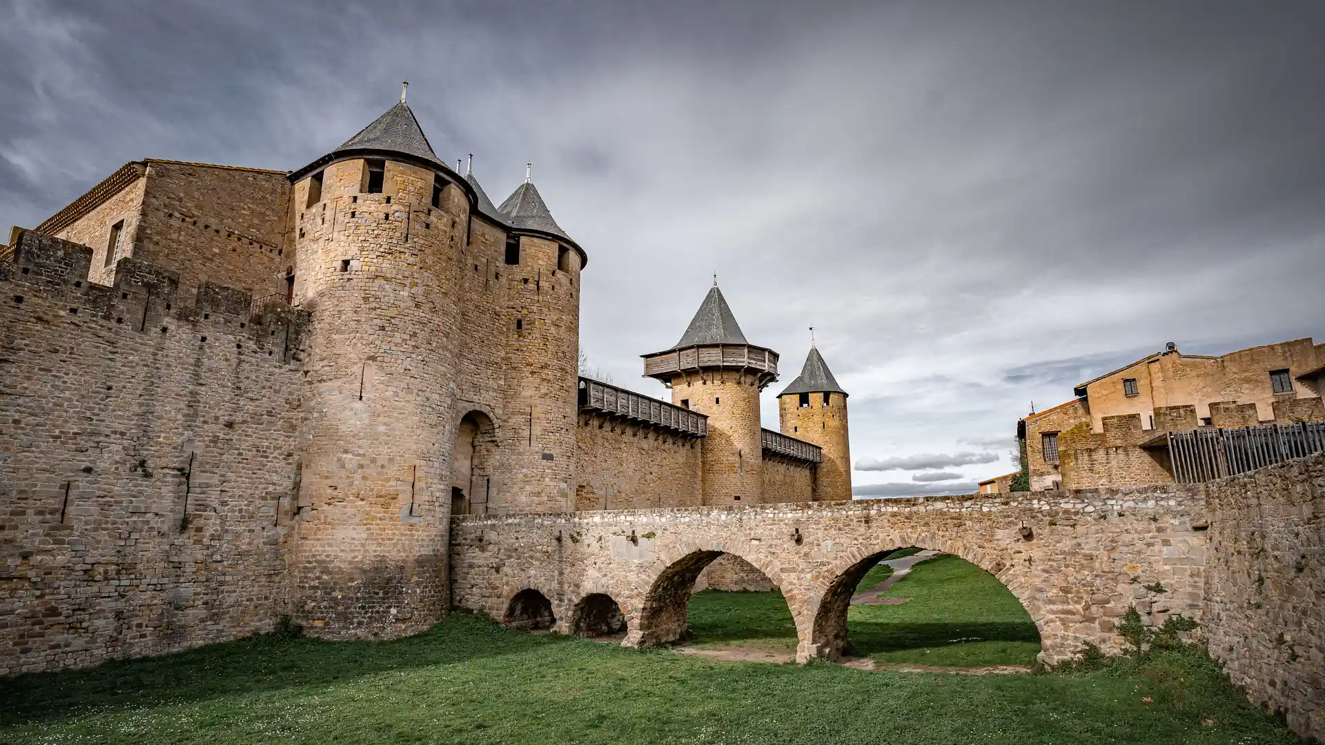 The round towers and conical slate roofs of the Château Comtal in the Cité de Carcassonne, reached by an arched stone bridge across the grassy ditch
